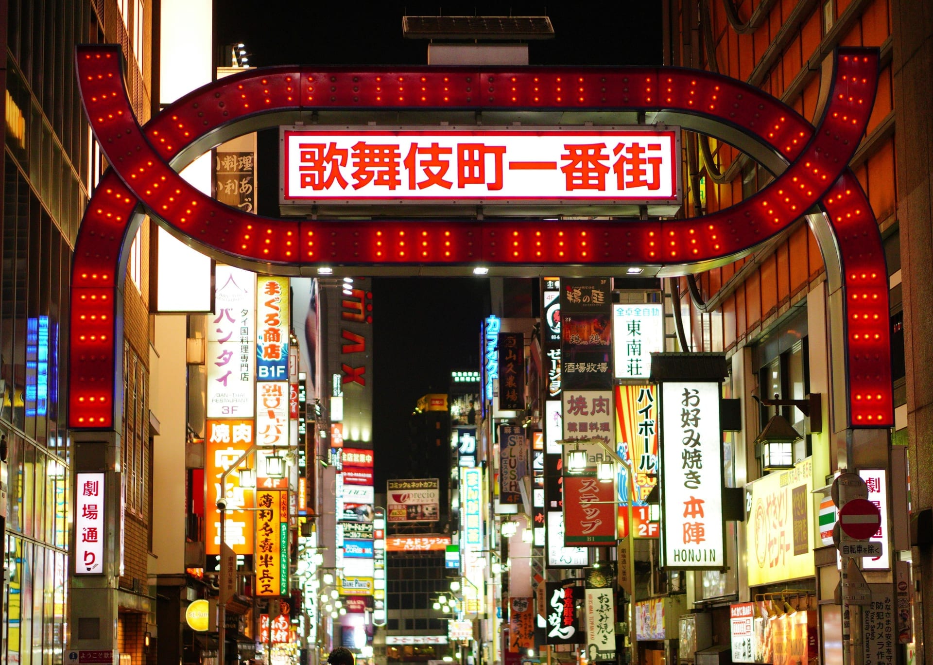 Kabukicho entertainment district entrance arch glowing with red neon lights and Japanese signs at night in Shinjuku